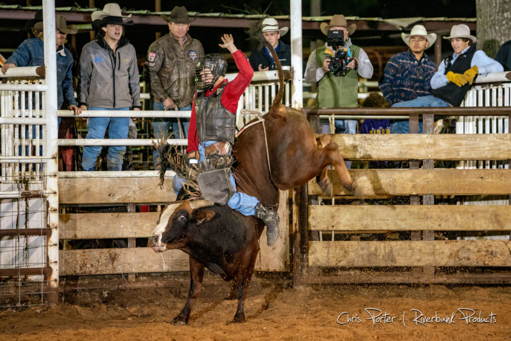 Bull rider on bucking bull with cowboys standing behind the bucking chutes